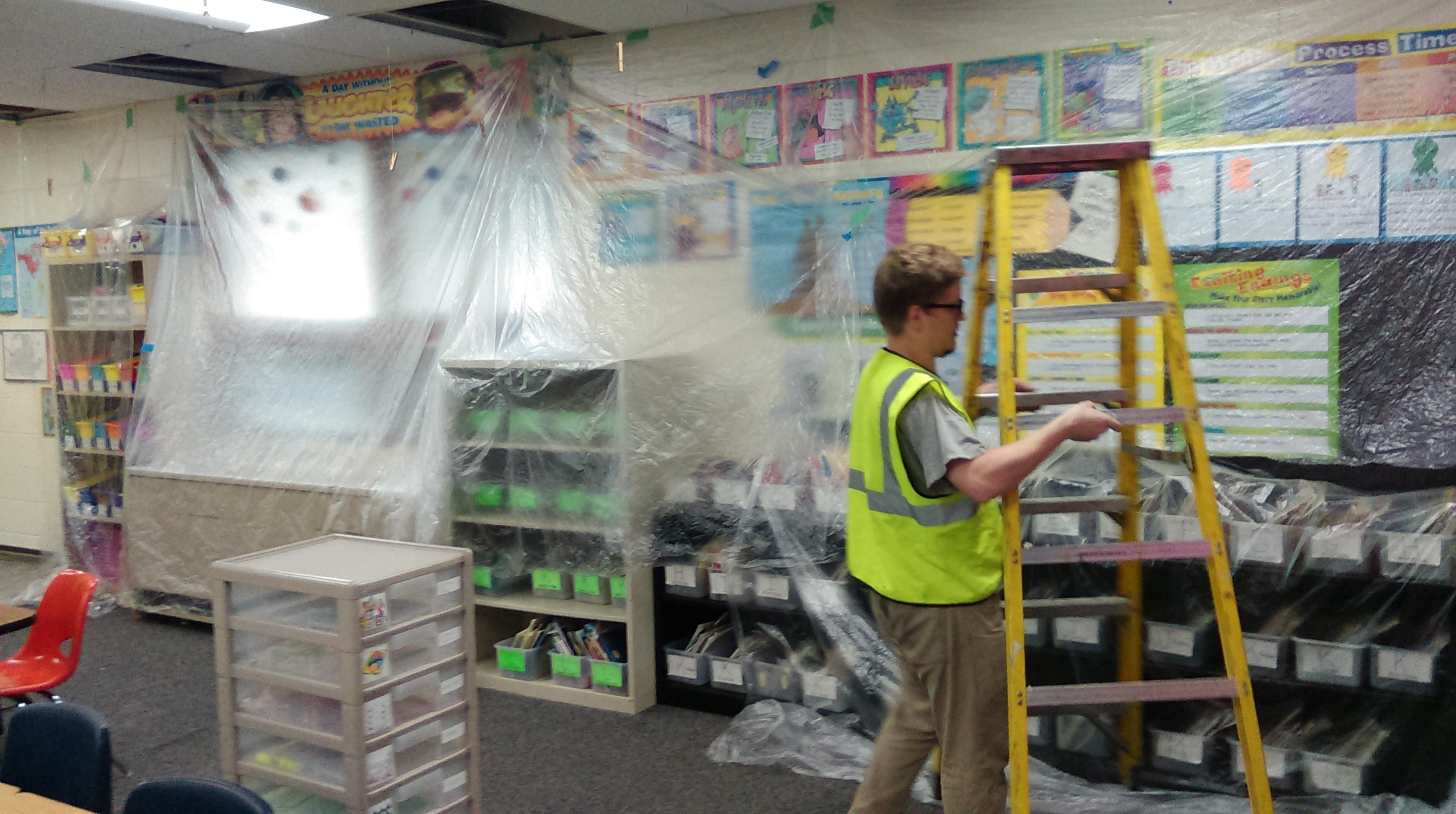 Accurate-Airtight Exteriors worker putting plastic up in a classroom to keep everything clean