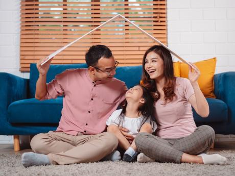 Happy family holding a model roof over their head as they sit and laugh in a living room Happy family holding a model roof over their head as they sit and laugh in a living room