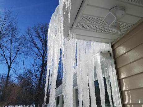 Large Icicles Forming Off The Edge Of The Roof Of A Home In Winter