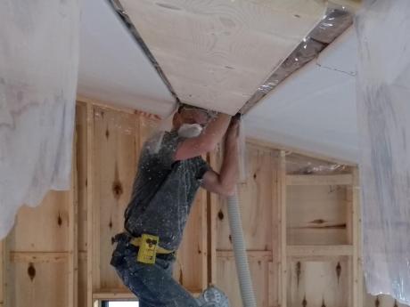 Crew Member Installing Blown Insulation Above Ceiling Tiles