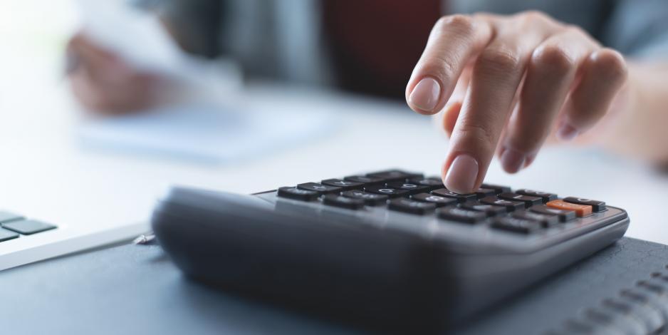 Hands typing on a calculator with financial papers on a desk