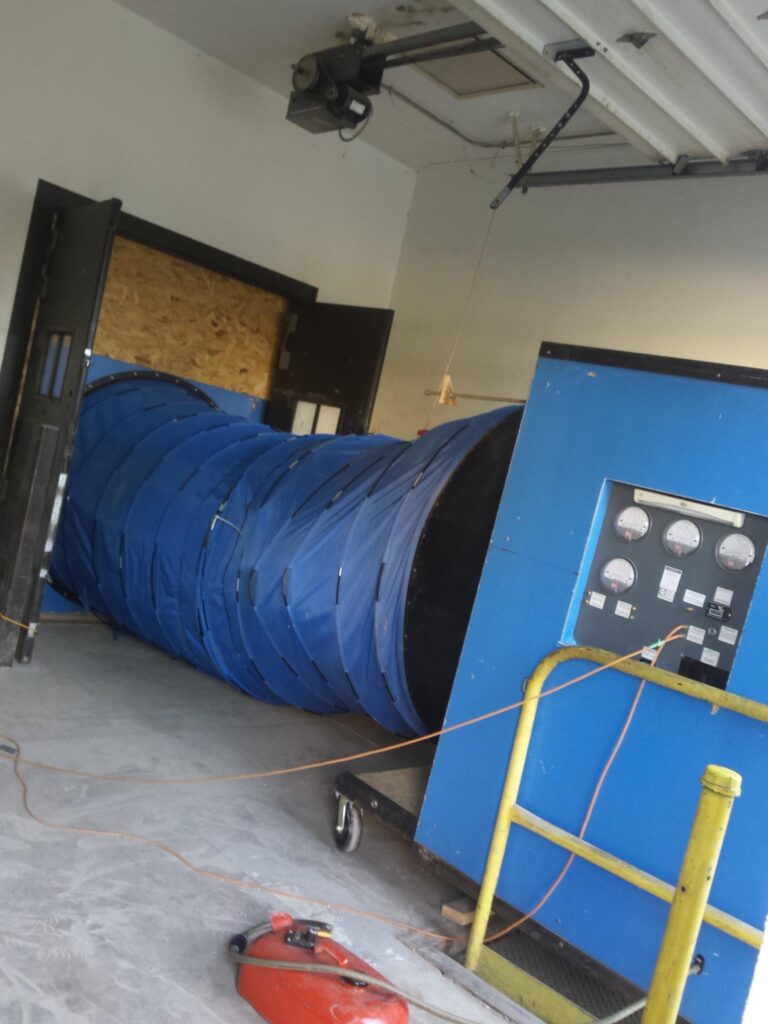 Snorkel of G54 blower door is inserted into an exterior building opening.